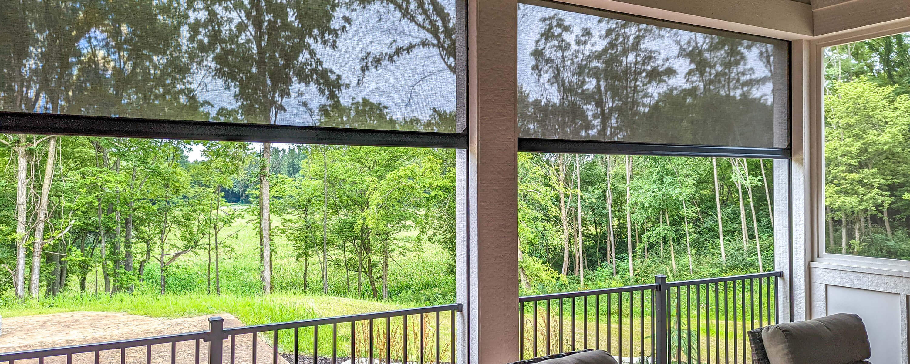Screened porch with railing and wooded view